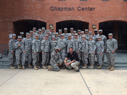 A group, all wearing camouflage, standing in front of a brick building named Chapman Center
